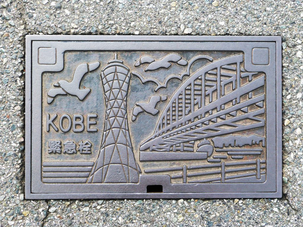 Plaque rectangulaire de la ville de Kobe sur laquelle sont représentées la tour du port et le grand pont ainsi que des mouettes